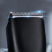 Close-up of a black electric hair clipper showing the silver metal cutting blades and guard, with a blue light glow effect and the STATUS logo in the bottom-left corner.