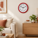 Champion red wall clock with white face mounted on a warm off-white living room wall beside natural wood furniture